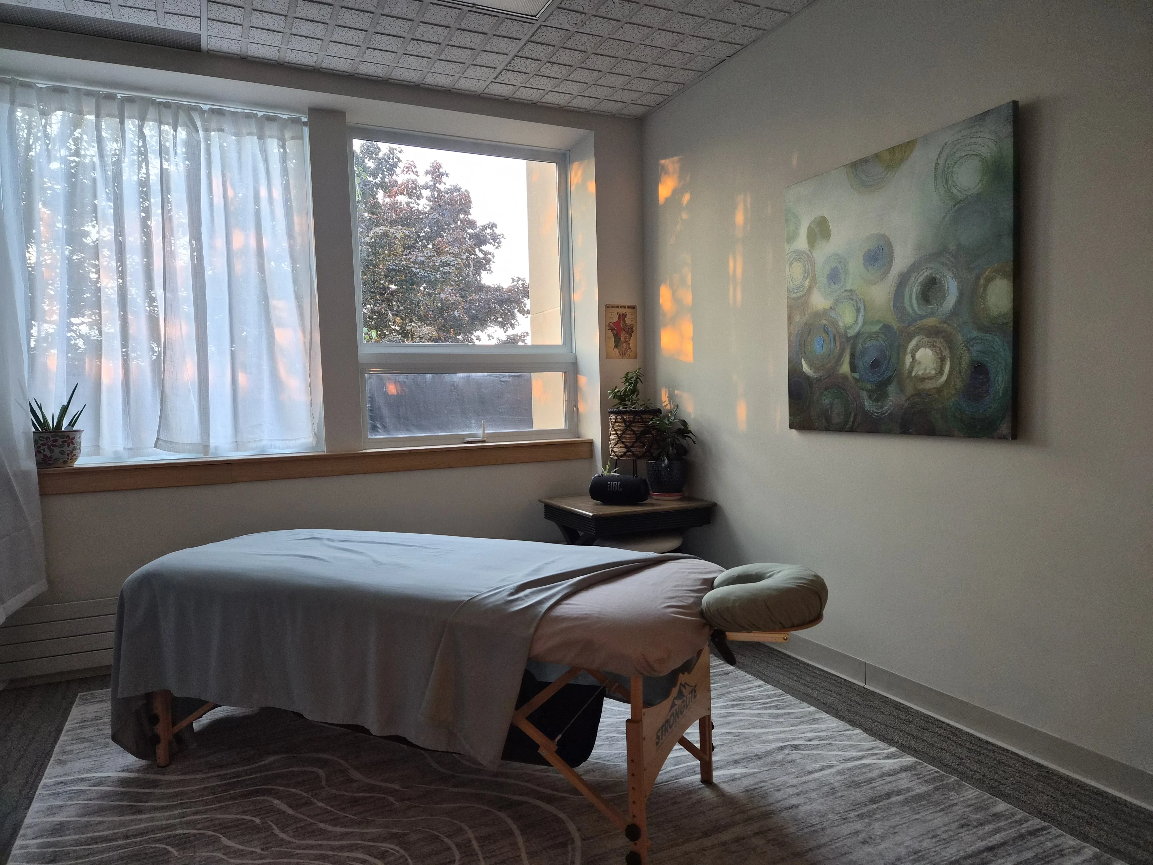 The treatment room with the massage table made up beside a curtained window, and a large abstract circle painting on the facing wall